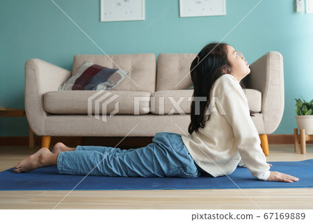 Asian little girl practicing yoga cobra pose on yoga mat in the living at home Asian little girl practicing yoga cobra pose on yoga mat in the living at home 67169889