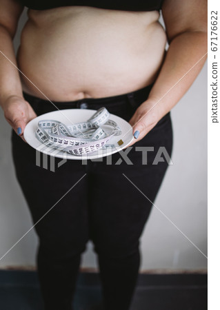 Overweight woman holding plate with measure tape Overweight woman holding plate with measure tape 67176622