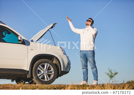 man standing near car with opened hood on sunset talking on phone calling assistance 67178172