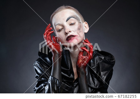 Portrait of horror woman in black raincoat with red hands near face 67182255