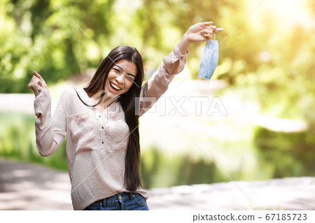 Joyful Asian Girl Celebrating End Of Quarantine, Removing Mask Outdoors, Copy Space Joyful Asian Girl Celebrating End Of Quarantine, Removing Mask Outdoors, Copy Space 67185723