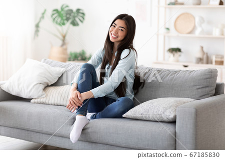Home Comfort. Beautiful Smiling Asian Girl Posing On Sofa In Living Room Home Comfort. Beautiful Smiling Asian Girl Posing On Sofa In Living Room 67185830