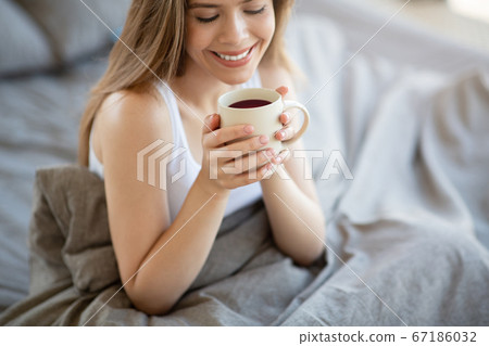 Smiling girl having cup of fresh coffee on bed in morning Smiling girl having cup of fresh coffee on bed in morning 67186032