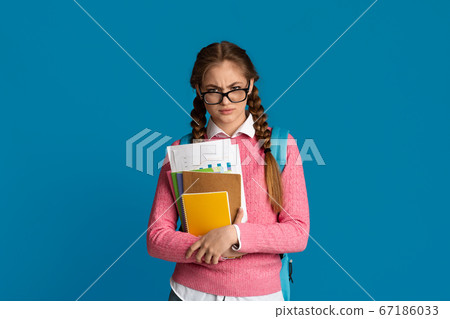 Displeased teenager girl with glasses on nose, looks disapprovingly and holds notebooks 67186033