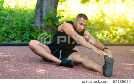 African American sportsman stretching his legs on jogging track at park 67186034