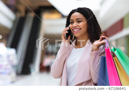 Black woman walking in mall with shopping bags and talking on cellphone 67186641