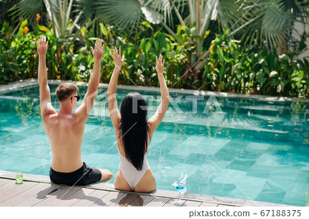 Happy couple sitting on pool edge Happy couple sitting on pool edge 67188375