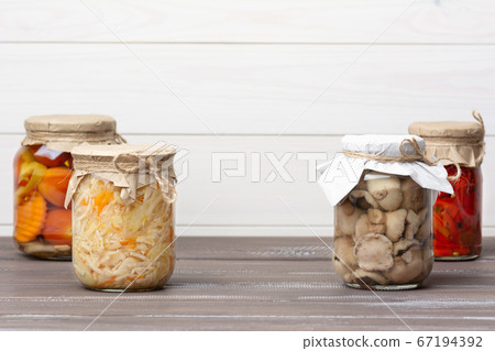Pickled fermented sauerkraut, tomatoes, peppers, carrots, mushrooms suillaceae, assorted in glass jars on a brown wooden table and white background. Pickled fermented sauerkraut, tomatoes, peppers, carrots, mushrooms suillaceae, assorted in glass jars on a brown wooden table and white background. 67194392