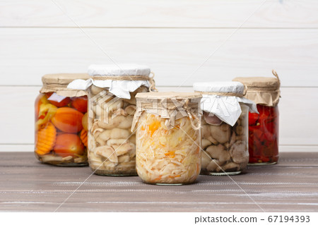 Pickled fermented sauerkraut, tomatoes, peppers, carrots, mushrooms suillaceae, assorted in glass jars on a brown wooden table and white background. Pickled fermented sauerkraut, tomatoes, peppers, carrots, mushrooms suillaceae, assorted in glass jars on a brown wooden table and white background. 67194393