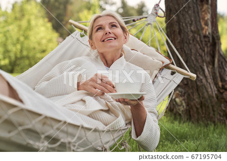 Jolly woman relaxing in open air with hot drink 67195704