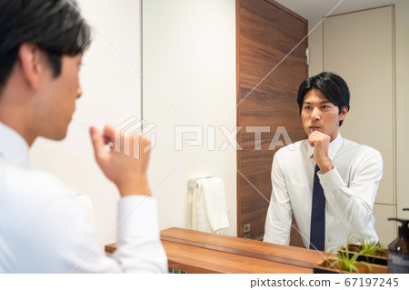 Young businessman brushing teeth in the bathroom Young businessman brushing teeth in the bathroom 67197245