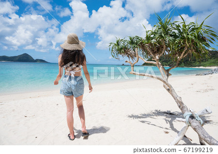 Rear view image of woman in straw hat standing on beautiful tropical beach 67199219