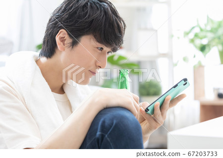 A young man watching a smartphone while drinking beer after taking a bath 67203733
