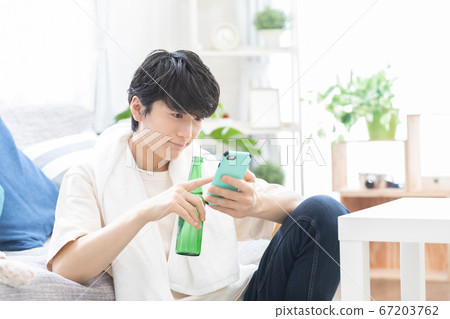 A young man watching a smartphone while drinking beer after taking a bath 67203762