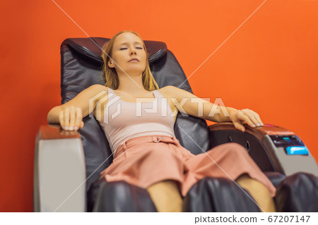 Beautiful young woman relaxing on the massage chair in airport or in the mall Beautiful young woman relaxing on the massage chair in airport or in the mall 67207147
