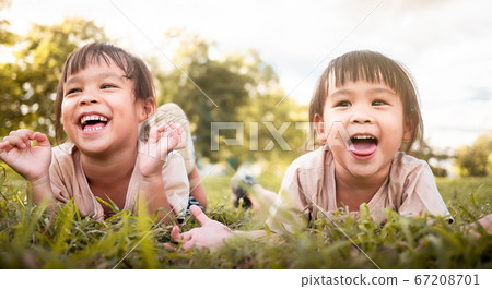 Two happy sibling girls lying on green grass 67208701