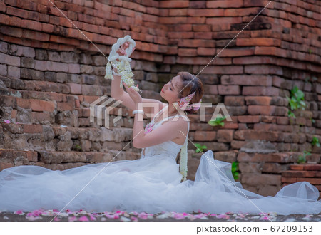 Pretty Asian Thai women holding beautiful garland in here hand and wearing traditional Thai dress costume according culture with the old brick wall at the ancient temple Chiangmai Thailand. 67209153