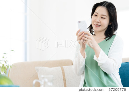 A middle woman who operates a smartphone in the living room 67209776