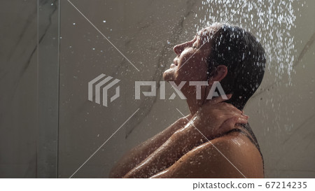 young woman runs hands on face standing under shower water young woman runs hands on face standing under shower water 67214235