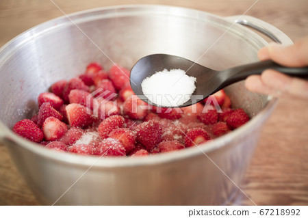 Female hand sprinkling sugar on a large amount of strawberries in a pan Female hand sprinkling sugar on a large amount of strawberries in a pan 67218992