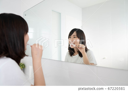 Young asian woman brushing her teeth in front of the bathroom mirror. Dental health care concept. Young asian woman brushing her teeth in front of the bathroom mirror. Dental health care concept. 67220381