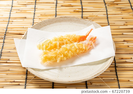 Two pieces of shrimp tempura on a sheet of tempura spread on a plate. 67220739