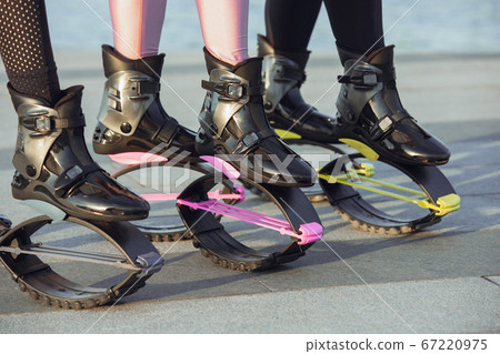 Beautiful women in sportswear jumping in a kangoo jumps shoes at the street on summer's sunny day 67220975