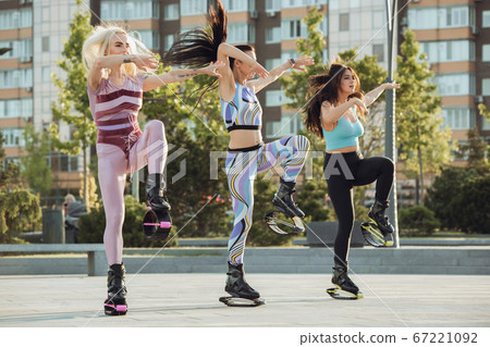 Beautiful women in sportswear jumping in a kangoo jumps shoes at the street on summer's sunny day 67221092