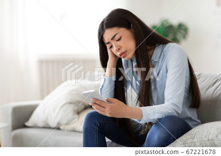 Waiting for his call. Upset asian girl sitting with cellphone at home 67221678