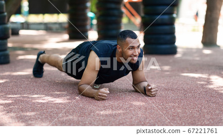 Strong black guy standing in elbow plank on road at park on sunny morning, empty space Strong black guy standing in elbow plank on road at park on sunny morning, empty space 67221761
