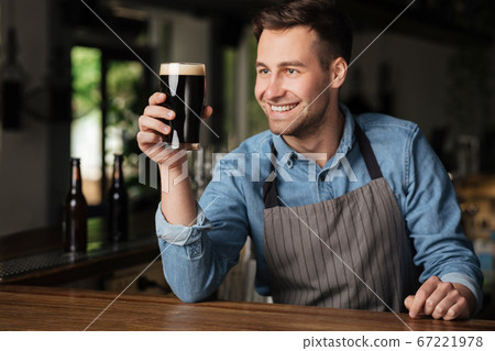 Great taste. Smiling handsome barman holds glass of dark beer in hand Great taste. Smiling handsome barman holds glass of dark beer in hand 67221978