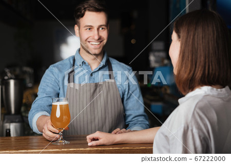 Beer for regular client. Smiling bartender gives to girl lager behind bar 67222000