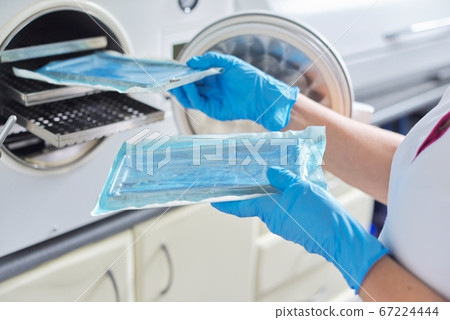 Female nurse doing sterilization of dental medical instruments in autoclave Female nurse doing sterilization of dental medical instruments in autoclave 67224444