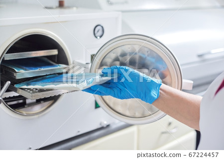 Female nurse doing sterilization of dental medical instruments in autoclave Female nurse doing sterilization of dental medical instruments in autoclave 67224457