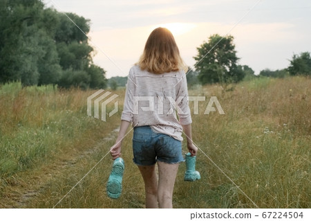 Teen girl walking on rural road with boots in hands 67224504