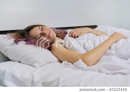 Teen girl waking up in the morning lying on pillow in bed Teen girl waking up in the morning lying on pillow in bed 67225450