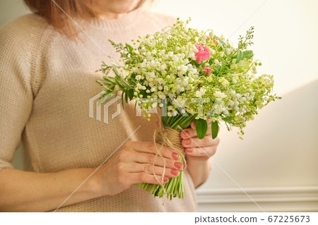 Beautiful fresh bouquet of lily of the valley flowers, pink rose, green branches in woman hand 67225673
