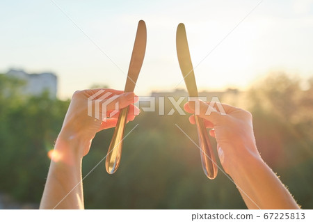 Two steel metal shiny knives in womans hand, background sunset 67225813