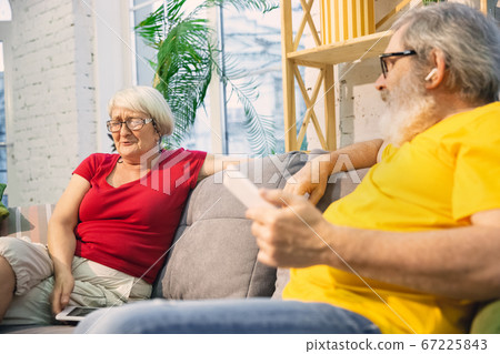 Couple of seniors spending time together being quarantined - caucasians mature and retired man and woman using modern gadgets, talking, drinking tea Couple of seniors spending time together being quarantined - caucasians mature and retired man and woman using modern gadgets, talking, drinking tea 67225843