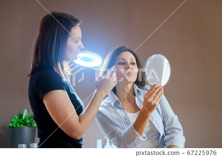 Middle-aged woman in beauty salon, talking to a beautician and looking at mirror 67225976