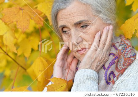 Close up portrait of sad senior woman in autumn park Close up portrait of sad senior woman in autumn park 67226110