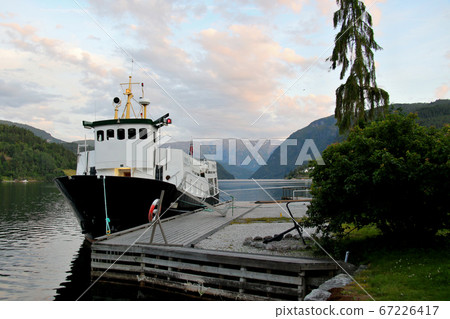 一艘小型遊船在午夜的陽光下依at在挪威哈當厄爾峽灣烏爾維克酒店東南部的碼頭上 67226417