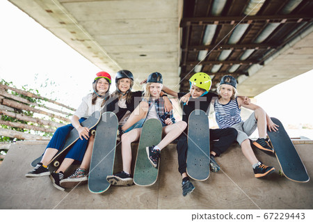Group of friends children at skate ramp. Portrait of confident early teenage friends hanging out at outdoor city skate park. Little skateboarders posing with boards from above on ramp in skate park Group of friends children at skate ramp. Portrait of confident early teenage friends hanging out at outdoor city skate park. Little skateboarders posing with boards from above on ramp in skate park 67229443
