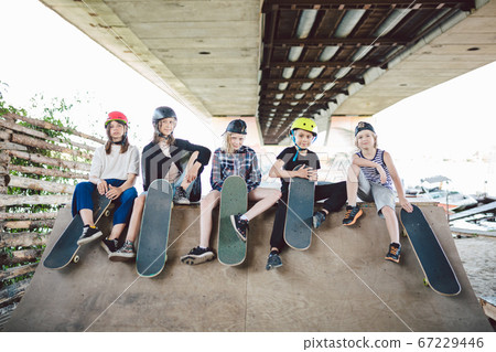 Group of friends children at skate ramp. Portrait of confident early teenage friends hanging out at outdoor city skate park. Little skateboarders posing with boards from above on ramp in skate park 67229446