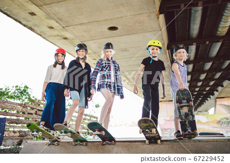 Group of friends children at skate ramp. Portrait of confident early teenage friends hanging out at outdoor city skate park. Little skateboarders posing with boards from above on ramp in skate park Group of friends children at skate ramp. Portrait of confident early teenage friends hanging out at outdoor city skate park. Little skateboarders posing with boards from above on ramp in skate park 67229452