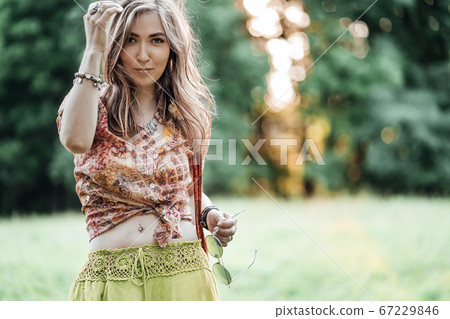 Portrait of Beautiful young woman wearing bohostyle clothes posing in the rays of the evening sun, sunset. Boho style fashion, female wearing silver jewelry having fun in park outdoors. Portrait of Beautiful young woman wearing bohostyle clothes posing in the rays of the evening sun, sunset. Boho style fashion, female wearing silver jewelry having fun in park outdoors. 67229846