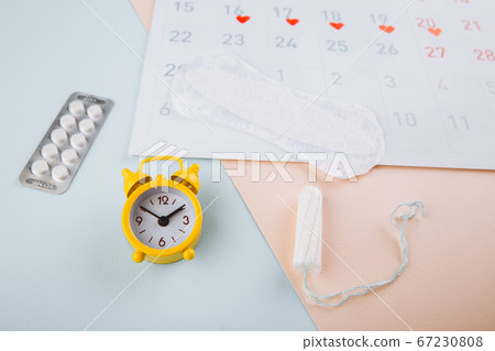 Calendar, cotton tampon and yellow alarm clock on blue pink background. Female's menstrual cycle concept 67230808