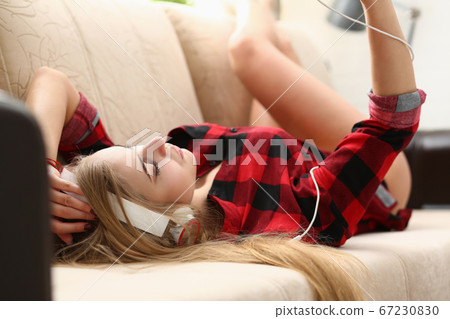 Pretty young lady listening music and lying on sofa Pretty young lady listening music and lying on sofa 67230830