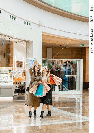 Shopping and entertainment, mall inside. Two beautiful girls with paper bags at the mall. The joy of consumption, Gift shopping, holiday. Shopping and entertainment, mall inside. Two beautiful girls with paper bags at the mall. The joy of consumption, Gift shopping, holiday. 67231655