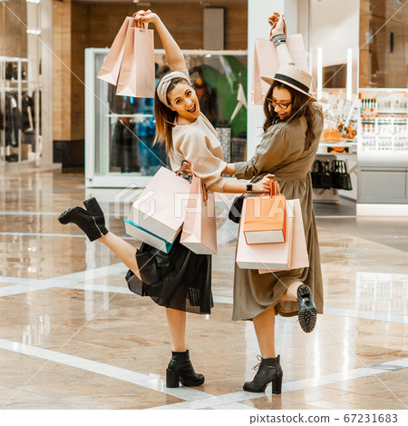 Shopping and entertainment, mall inside. Two beautiful girls with paper bags at the mall. The joy of consumption, Gift shopping, holiday. 67231683
